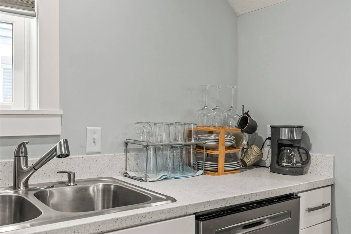 Wide view of the kitchen counter showcasing the sink, dishwasher, dish rack, coffee maker, and ample prep space.