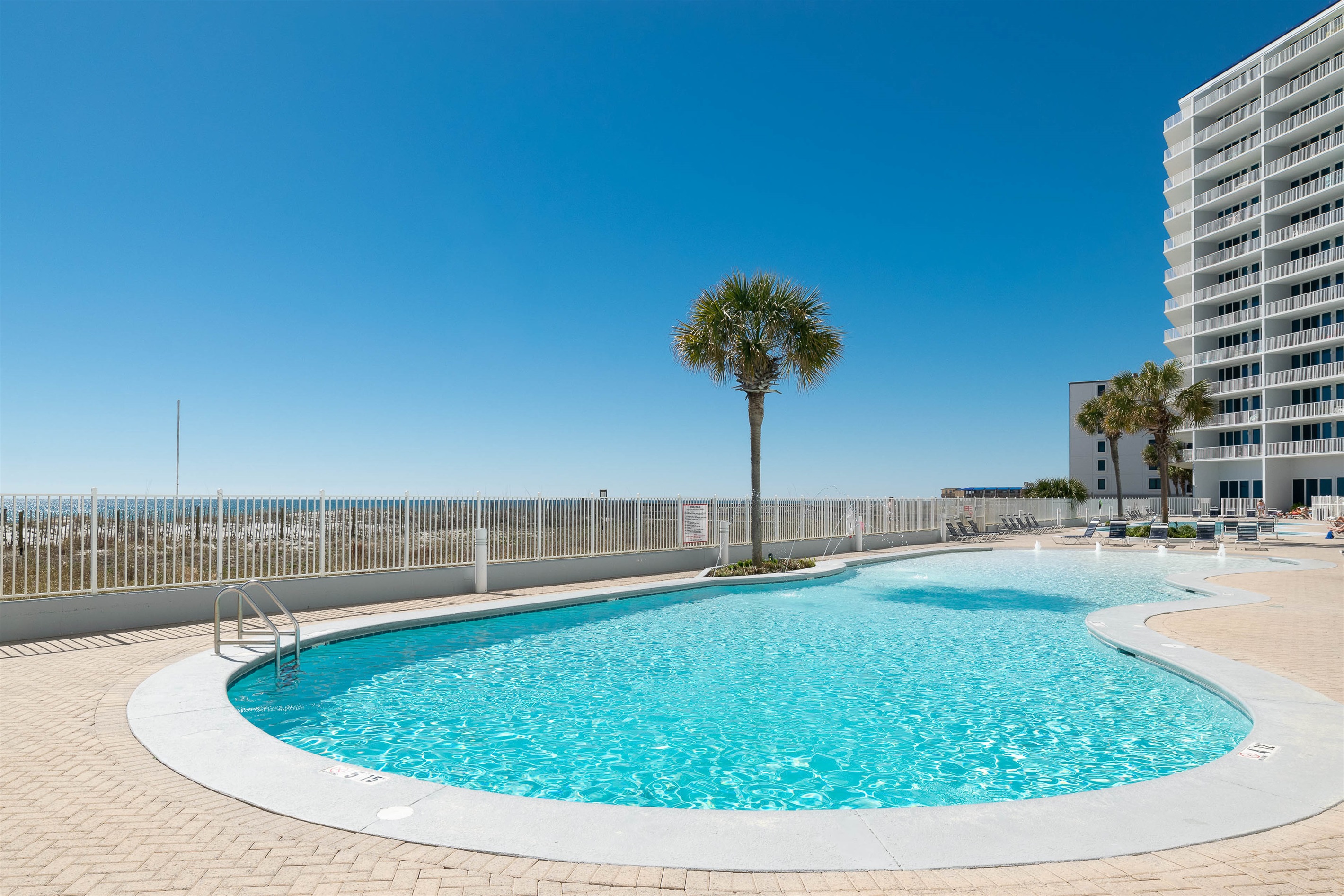 Relax by the shore! Our Gulf Shores vacation rental features a massive outdoor pool with ample lounge seating and direct private beach access.