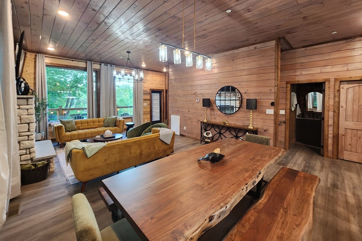 Spacious dining and living area surrounded by natural wood finishes and large windows.