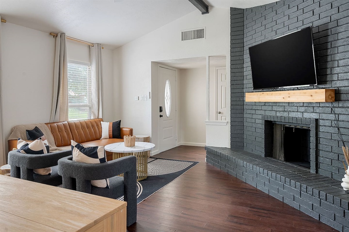 Step into this cozy living area featuring a stylish brick fireplace and a mounted flat-screen TV. The room is designed for comfort with a sofa and armchairs.