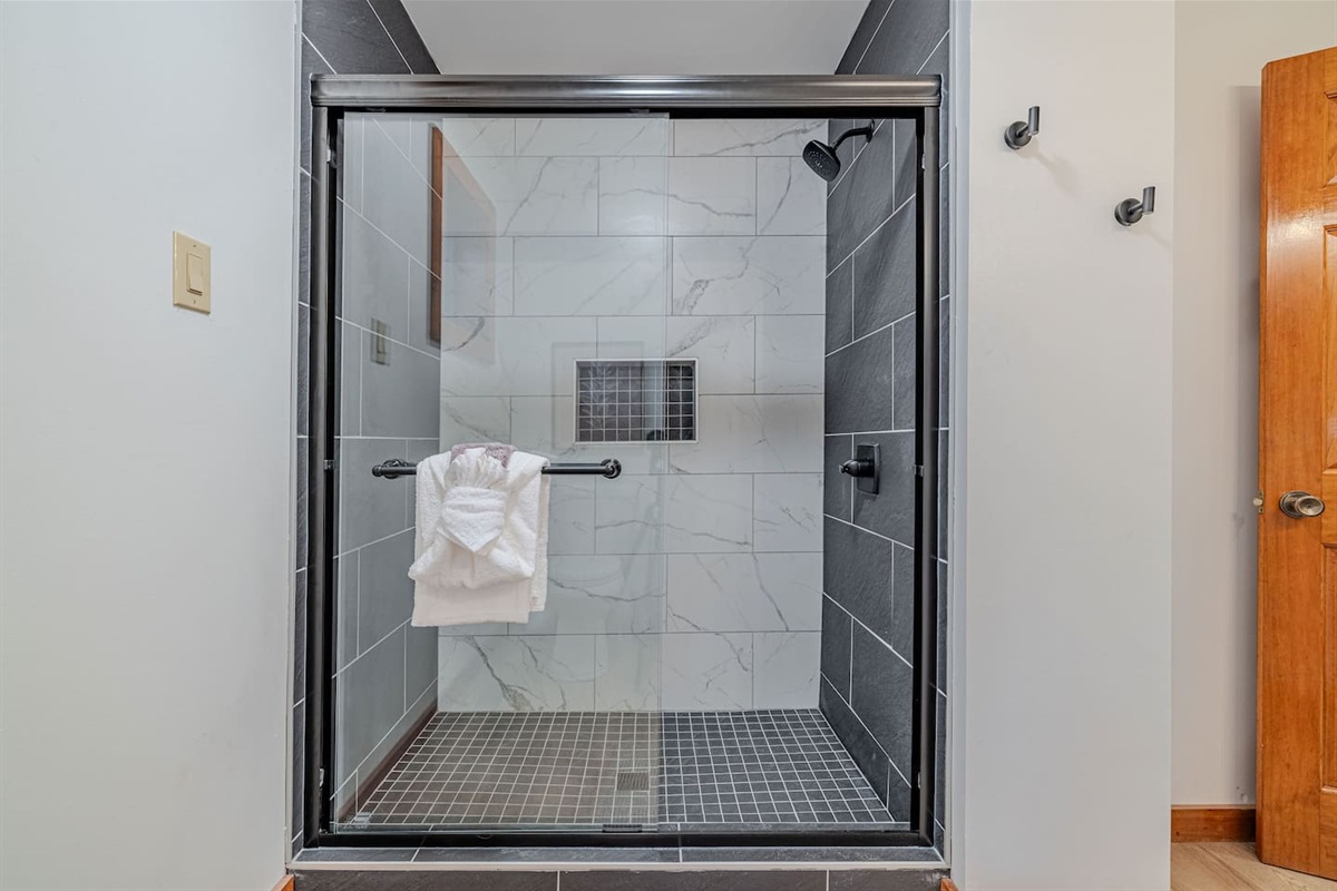 A stunning walk-in shower wrapped in rich black and marble-inspired tile creates a bold, spa-worthy statement within the primary bath.