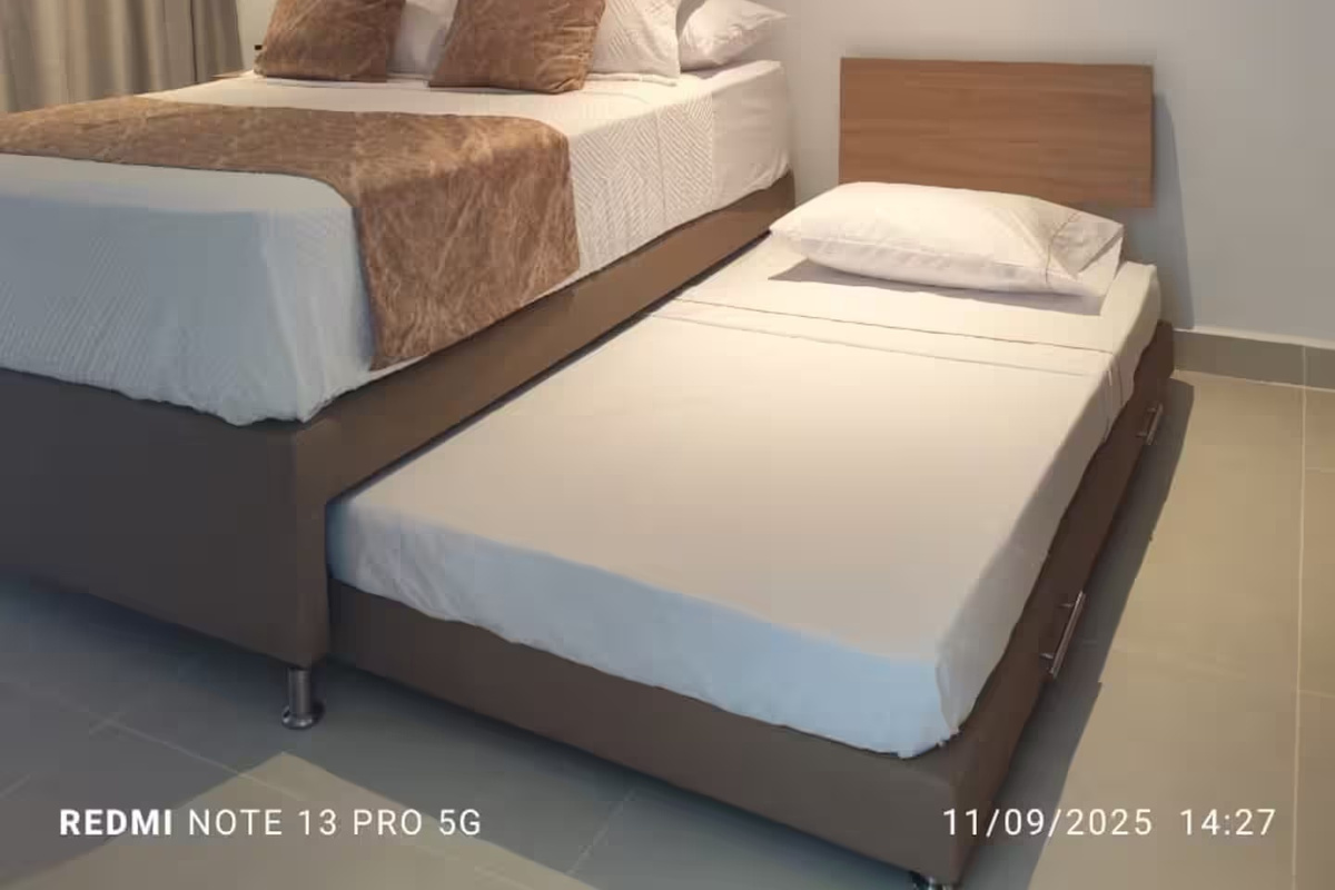 Dormitorio con cama principal, cama nido individual extraíble, armario empotrado y espacio de escritorio, ofreciendo opciones flexibles para dormir y guardar pertenencias.