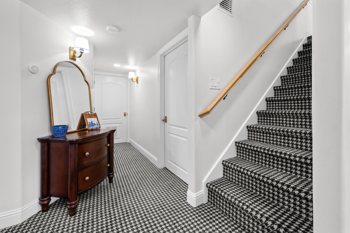 A thoughtfully styled hallway features elegant wall lighting, a statement mirror, and a distinctive patterned carpet that adds character throughout the lower level.