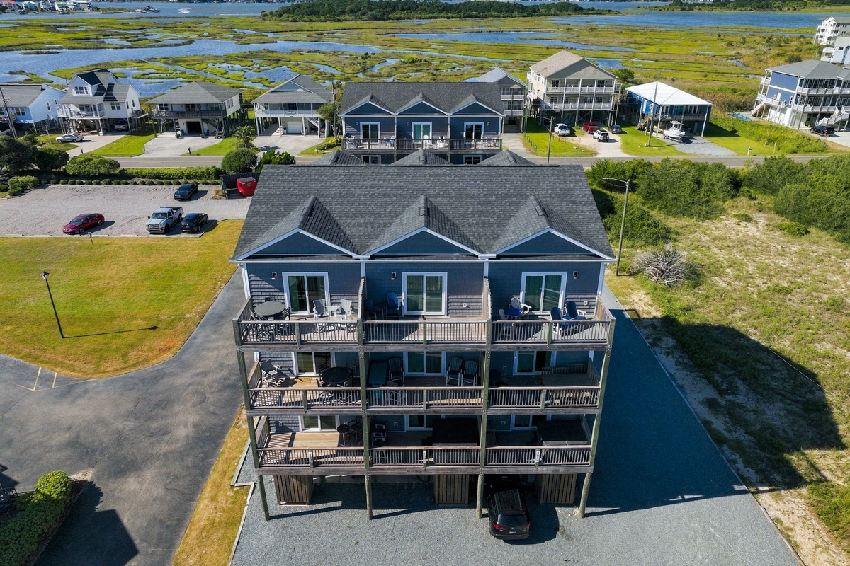 High-angle aerial shot capturing the full elevation of the beachfront townhouse complex, highlighting multi-tier private balconies and surrounding coastal landscape view.