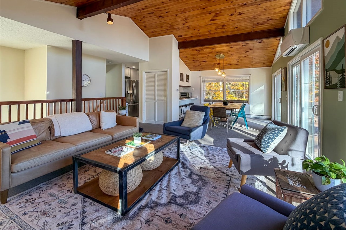The open plan living and dining area on the second floor adjoins a galley kitchen. Sliding doors open up to a deck with a grill, dining set, and fire pit with Adirondack chairs.
