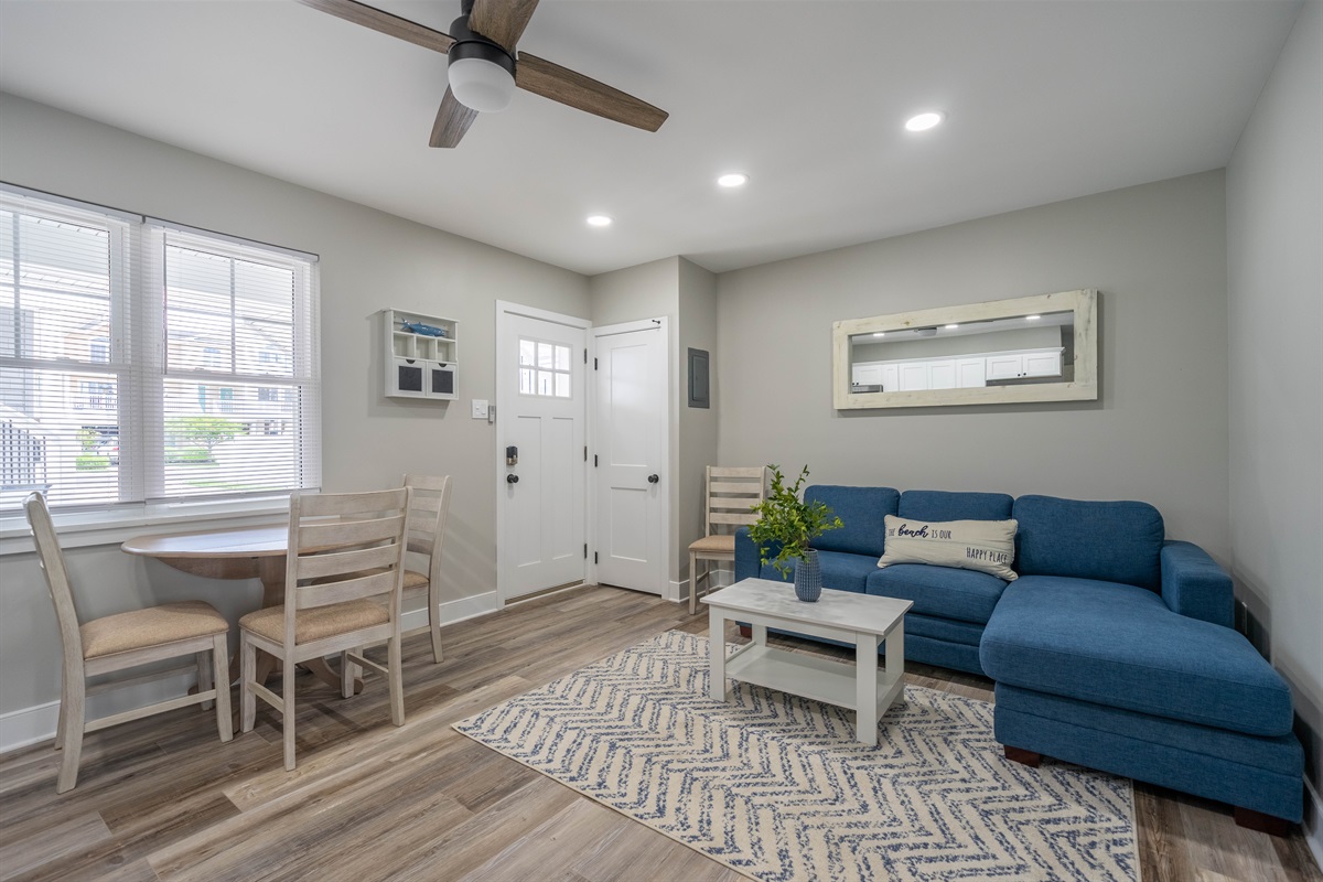 Open living area with comfortable seating, ceiling fan, and soft natural light. A small dining nook by the window and neutral finishes create a relaxed space for unwinding, sharing meals, or spending time together indoors.