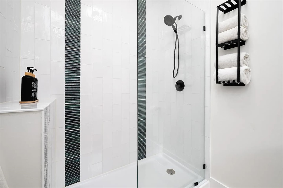 Sleek, spa-inspired bathroom featuring a glass-enclosed walk-in shower, contemporary matte-black fixtures, crisp white tile, and plush towel storage designed for comfort, cleanliness, and a luxury stay.