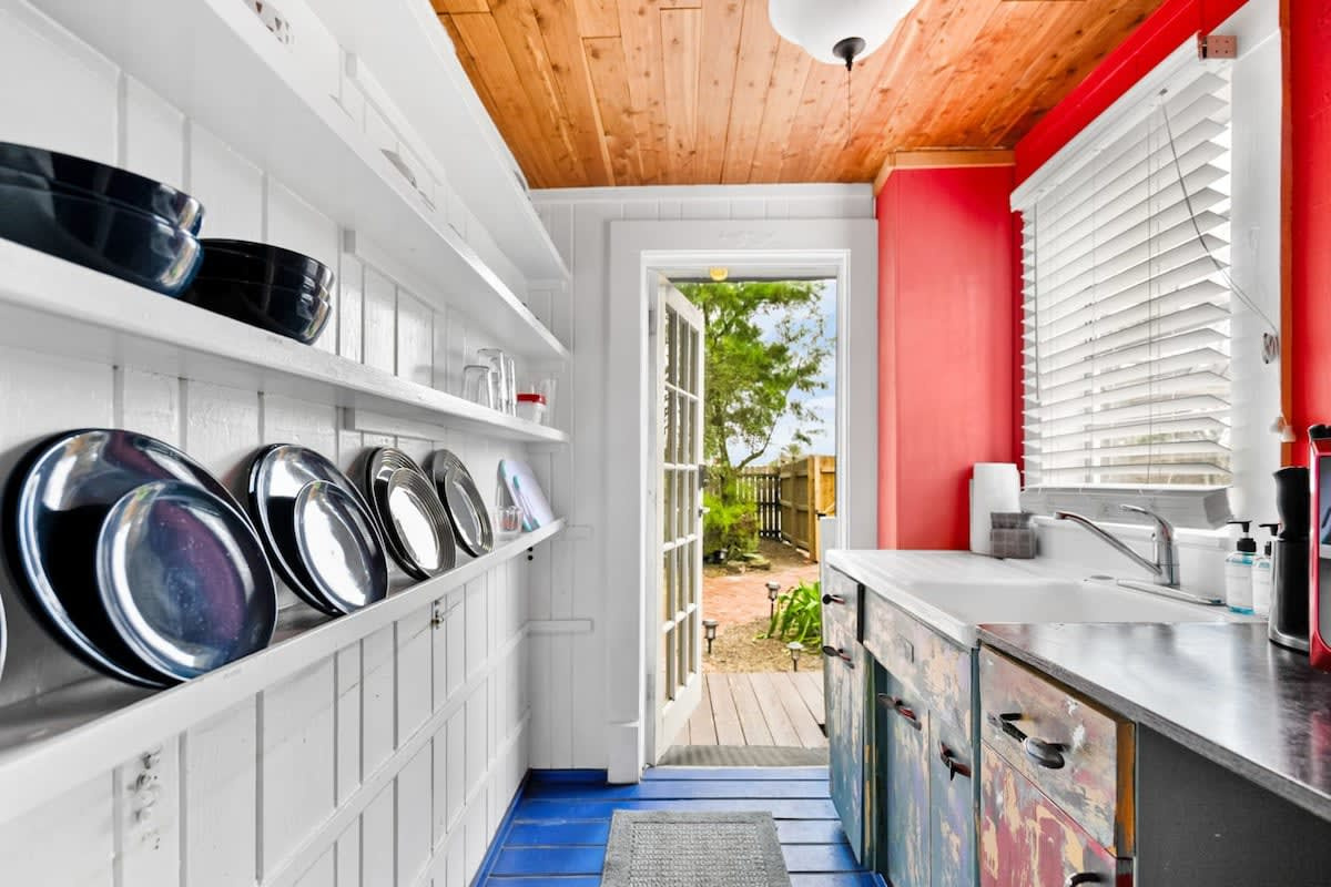 The galley kitchen runs the length of the room, with dishes stacked on open shelves and the door standing open to the patio. Small and characterful, and set up so that everything is exactly where you can see it.