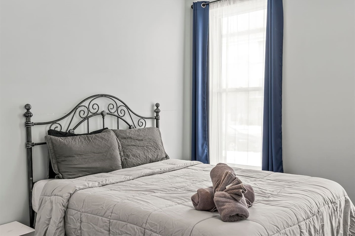 Primary bedroom view highlighting the ornate metal headboard and large window with blackout curtains.