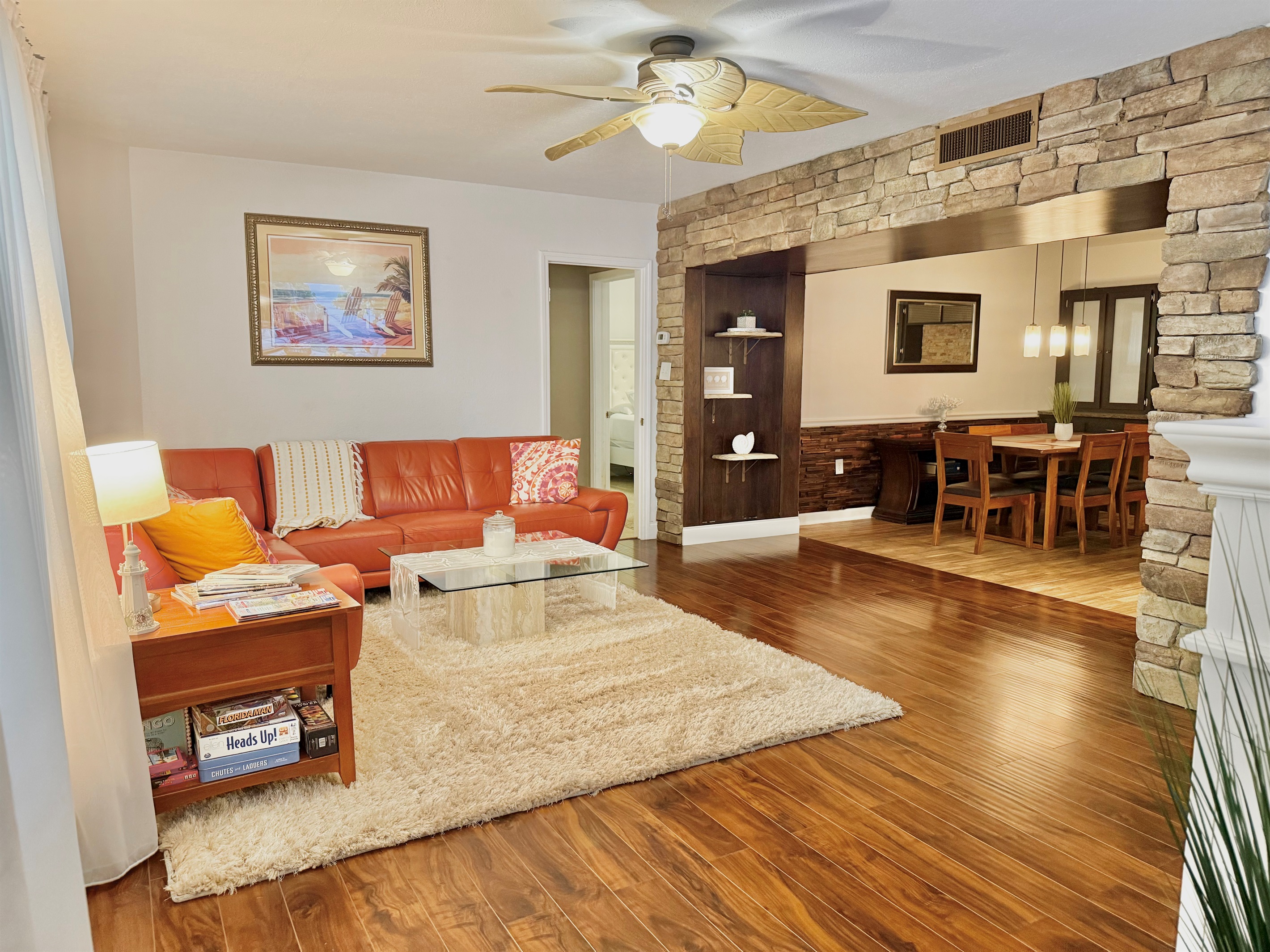 With bold burnt-orange seating, glass-top coffee table, and a shag rug underfoot, this space blends retro flair with modern comfort.