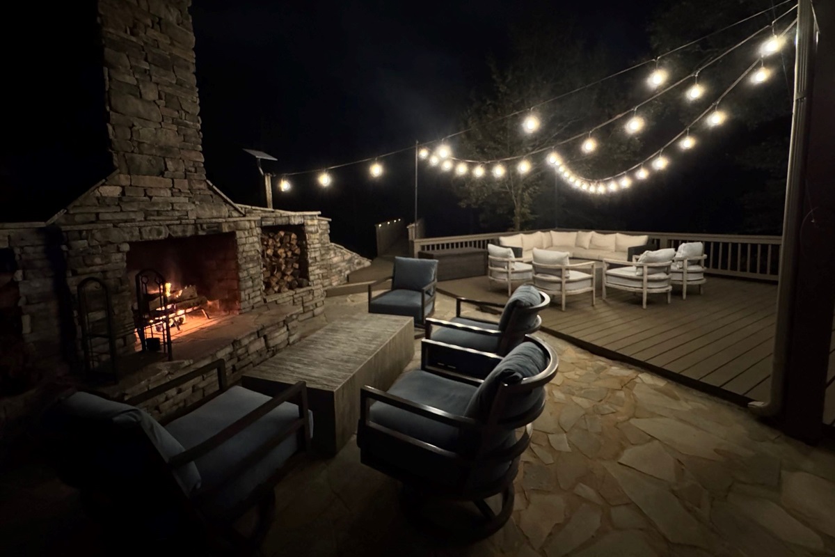 Enjoy party lights at night around the outdoor fireplace, creating a warm and inviting atmosphere for evening gatherings by the lake.