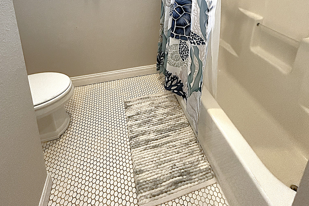 Sparkling clean bathroom with tub/shower combo, beadboard accents, and coastal-inspired decor. This well-appointed shared bathroom serves the bunk room and common areas with style and function