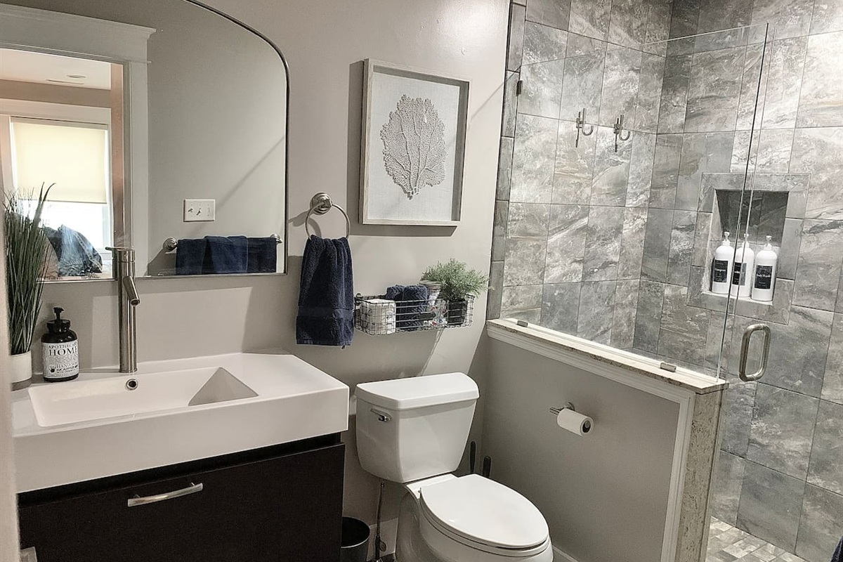 Refresh in this sleek bathroom featuring a modern vanity and a custom glass-enclosed shower with elegant grey tiling. Coastal artwork and a minimalist design create a spa-like atmosphere for your morning routine.