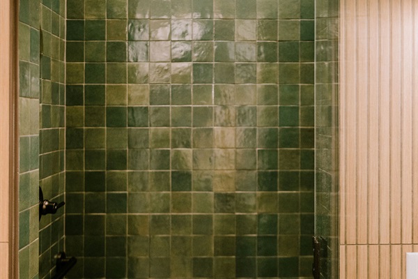 Roll-in tile shower at the Homestead Suite &mdash; ADA-accessible with step-free entry, finished in handcrafted green Hill Country tile at Gaines Ranch on the Square.