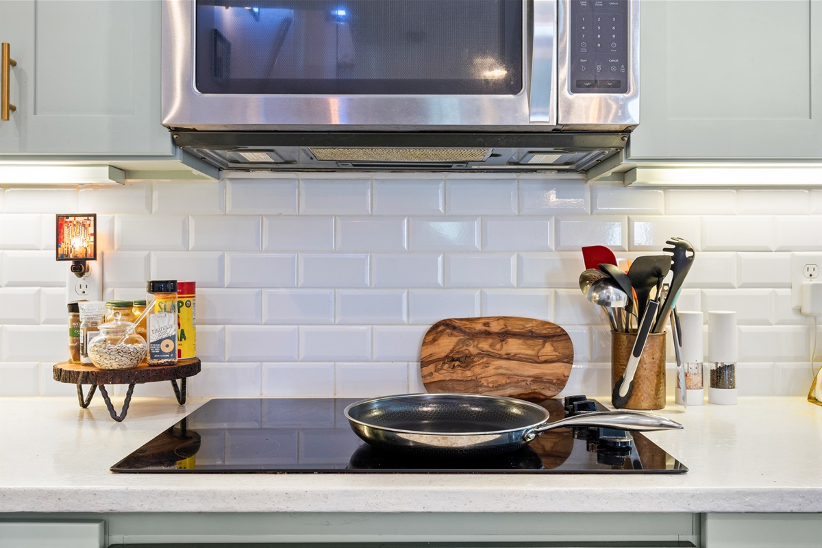 Modern stovetop with stainless pan, spice rack, and cooking utensils in fully equipped Jacksonville Beach rental kitchen.