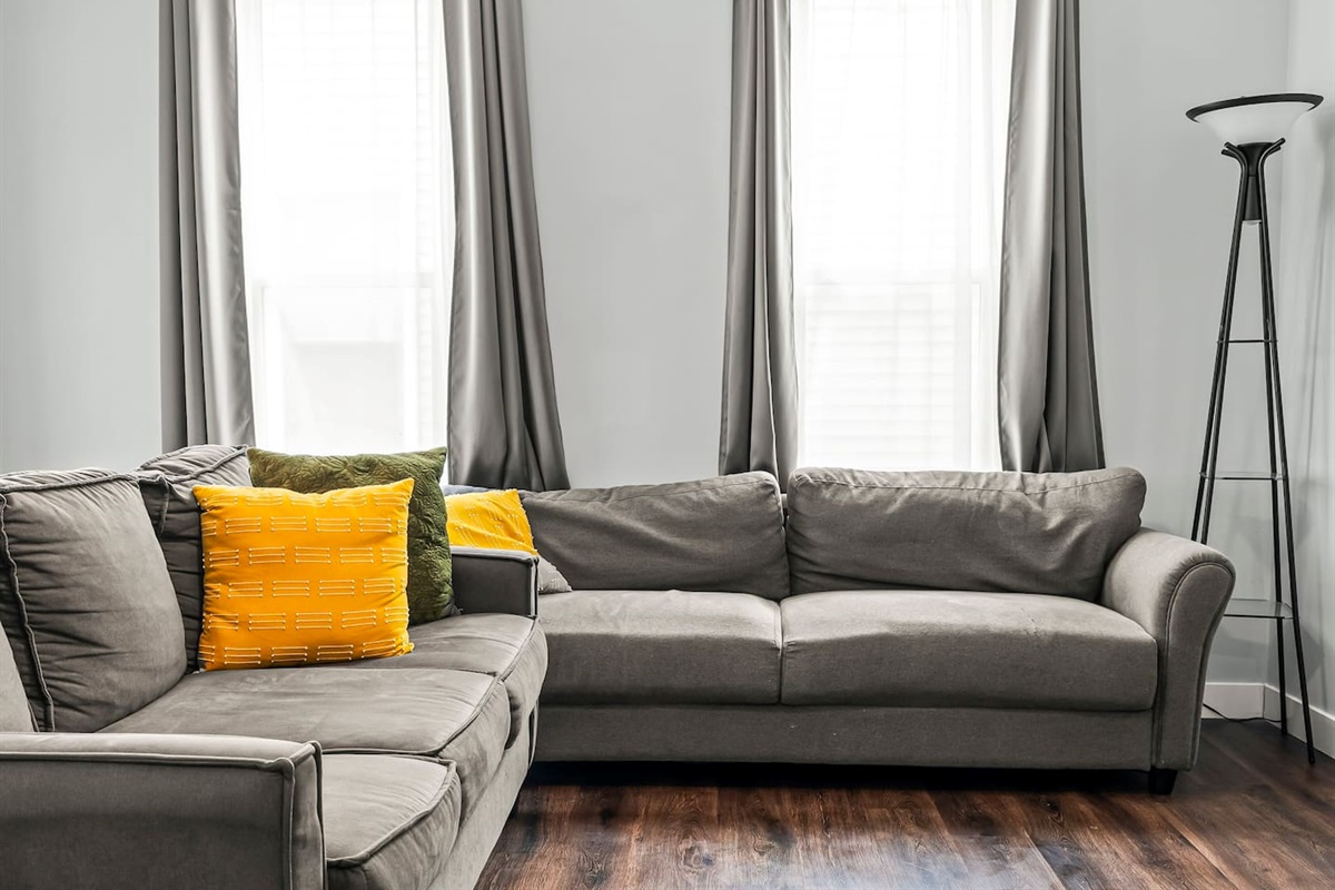 Bright and airy living room anchored by a spacious sectional, tall windows, and warm natural light.