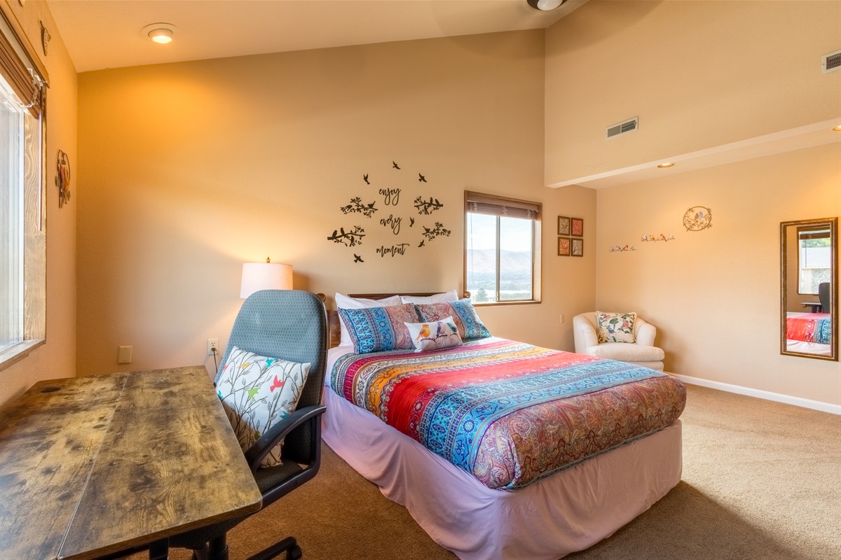 Large guest bedroom with sit stand desk and ceiling fan.