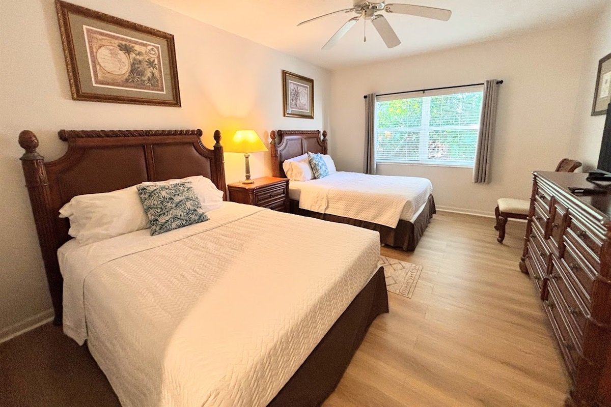 Comfortable bedroom featuring two beds, wood-look flooring, dresser storage, and plenty of natural light.
