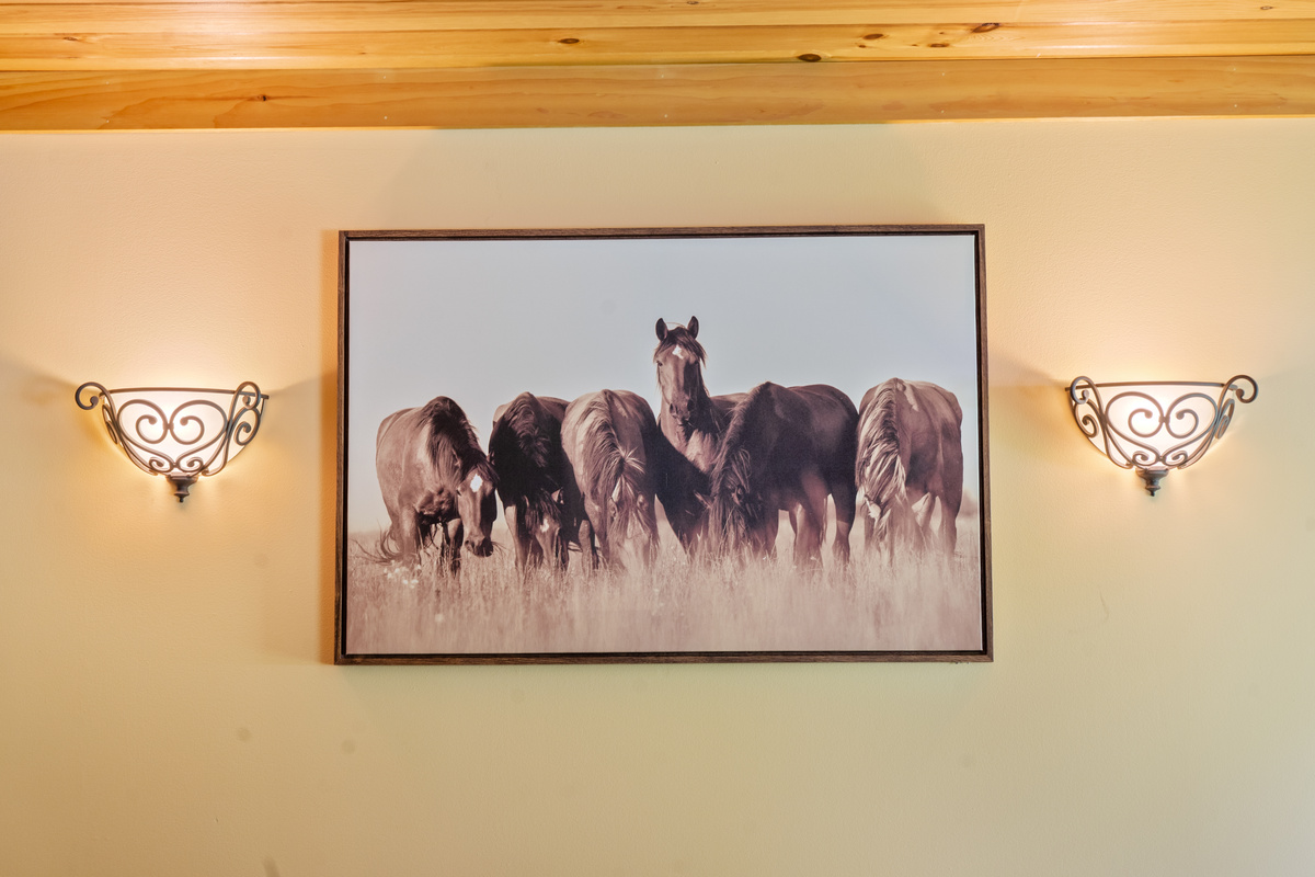 Admire the curated decor choices throughout the home, including this large horse-themed framed wall art. Positioned directly over the loveseat in the living room, the piece is highlighted by two elegant, scroll-work ambient light sconces.