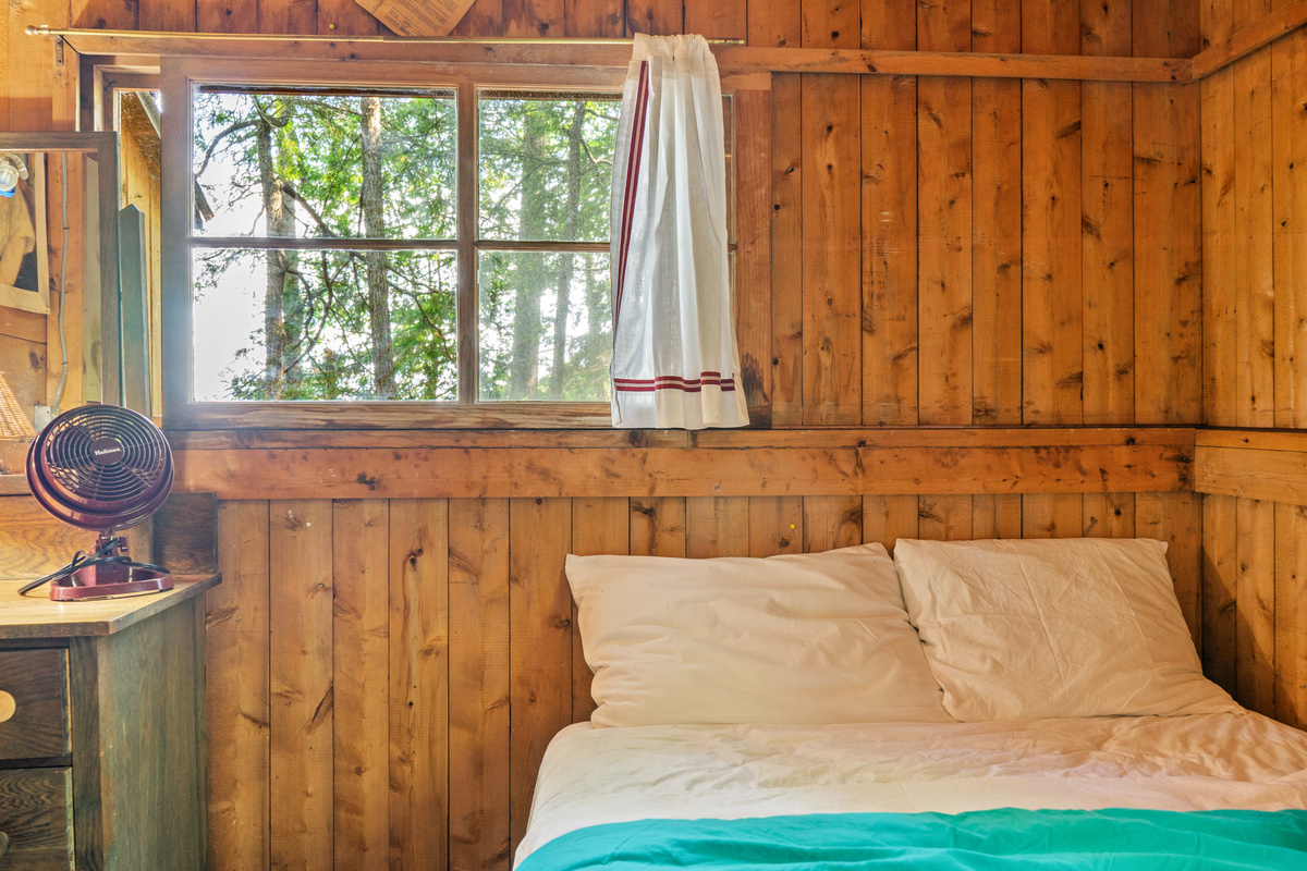 Cozy bed-side view in the guest room at Loonrise Point! Wake up to natural sunlight and direct sightlines to the dock through the window. Features full privacy walls & rustic charm on Beech Hill Pond in Otis, ME.