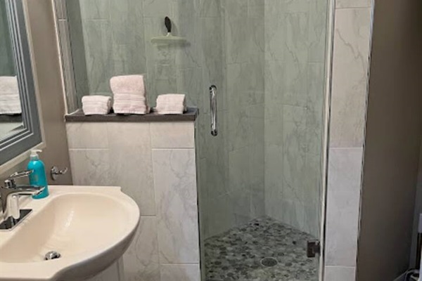Updated bathroom featuring a walk-in shower, modern tilework, vanity space, and clean neutral finishes.