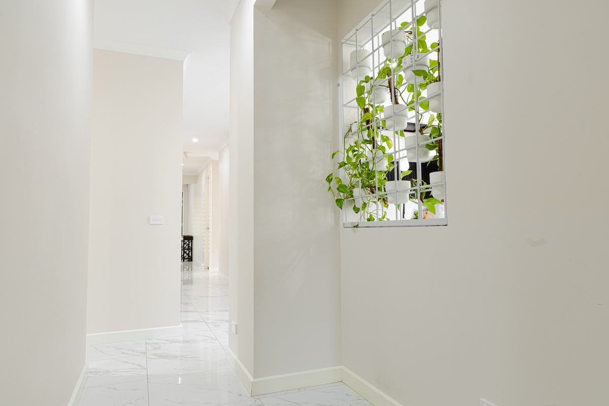 This hallway at Willows Stays Holiday adds a bright connection through the home, with gloss floor tiles and greenery bringing warmth to the entry flow.