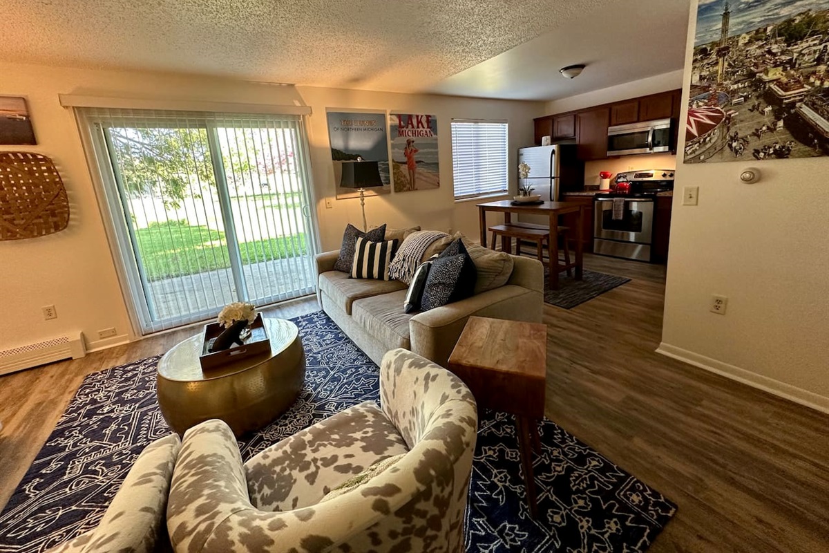 Enjoy a cozy, open-concept space with a comfy sofa, bold decor, and a fully stocked kitchen featuring stainless appliances. A bistro-style dining table, natural light, and charming Michigan art make this the perfect retreat for work or play.