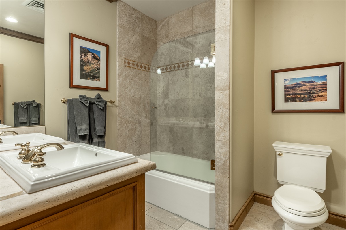 The Charming Chalet primary bathroom offers dual vanity, stone counters, tub/shower combo, and large mirror.