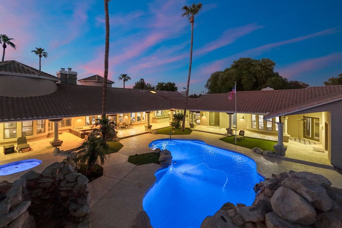 This expansive backyard transforms at dusk, with ambient lighting and a sparkling pool setting the mood.

