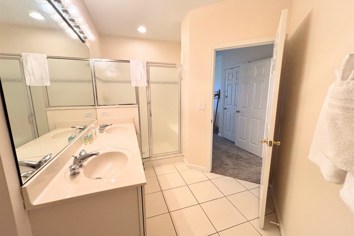 Bright bathroom with large vanity, full mirror, tile flooring, and a walk-in shower with glass doors.
