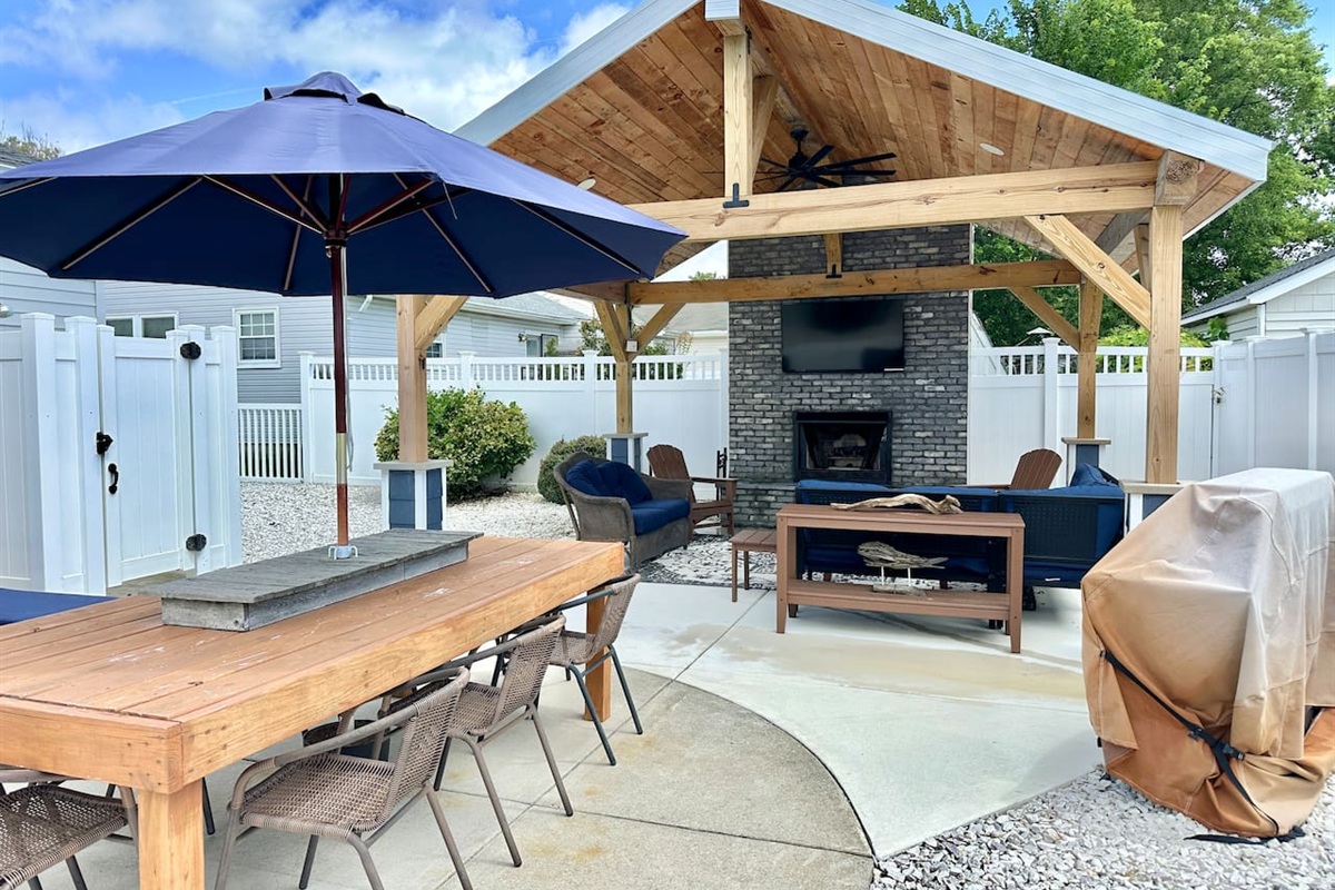 Savor alfresco meals at the spacious wooden dining table in your private backyard. This inviting space connects to a luxury covered lounge with a stone fireplace and TV, creating the ultimate setting for vacation entertaining.