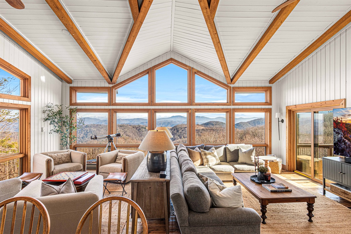 Light-filled great room with vaulted ceilings, exposed beams, and wall-to-wall windows framing sweeping mountain views—this is the heart of the home.