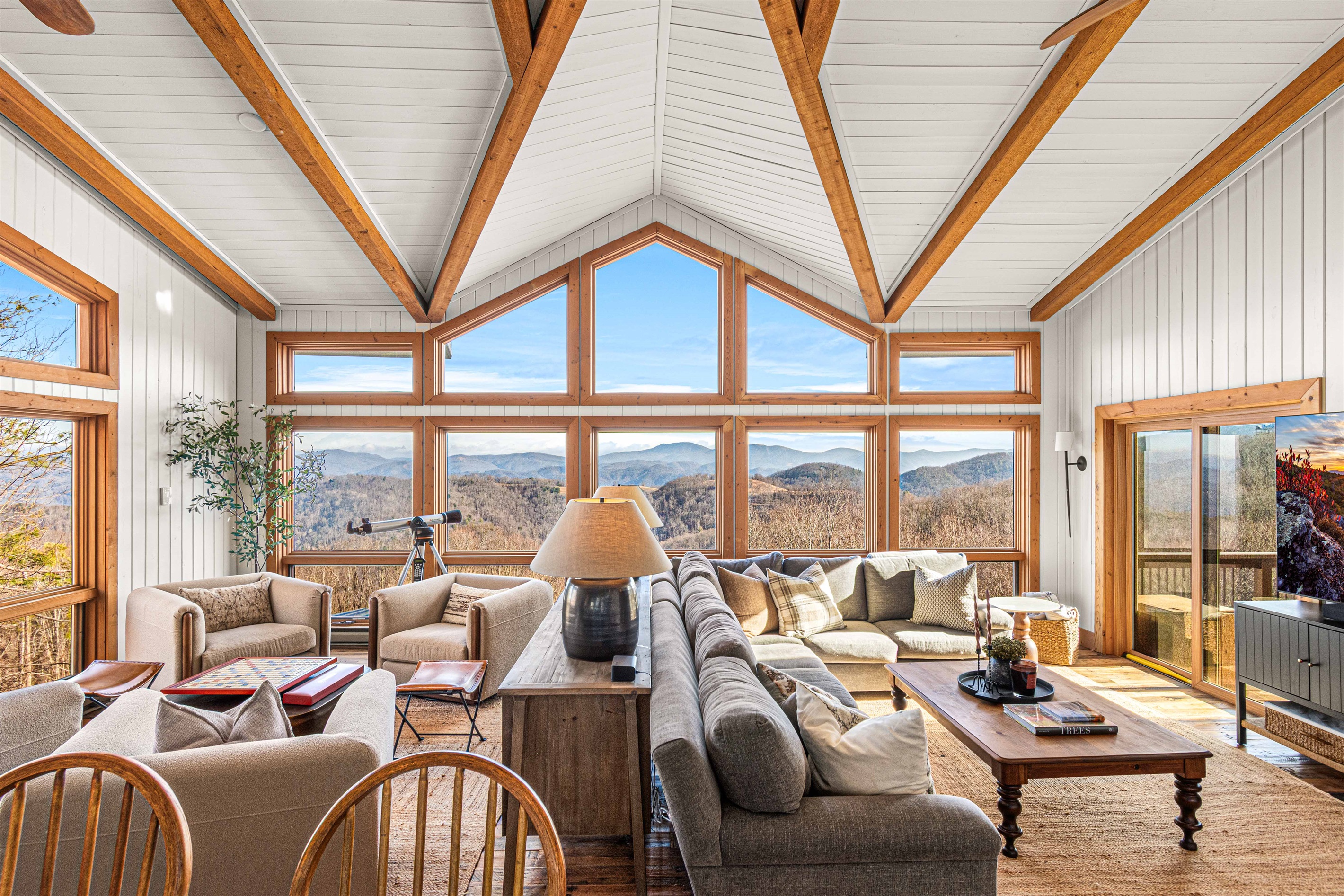 Light-filled great room with vaulted ceilings, exposed beams, and wall-to-wall windows framing sweeping mountain views—this is the heart of the home.