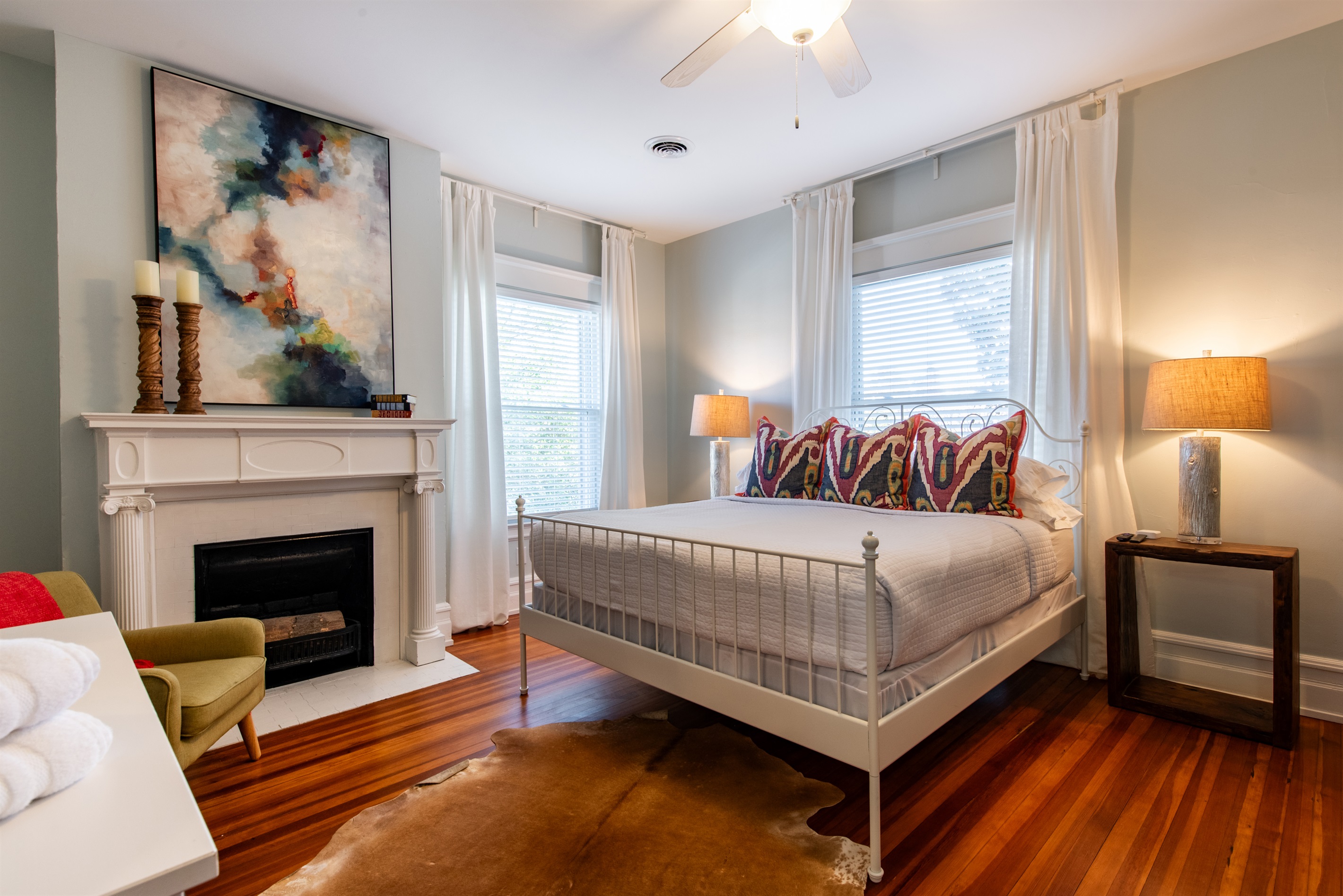 Rest easy in this serene bedroom on the Bourbon Trail in Louisville’s Highlands! Features a comfy bed with vibrant pillows, a decorative fireplace, & a cozy chair—ideal for a peaceful retreat