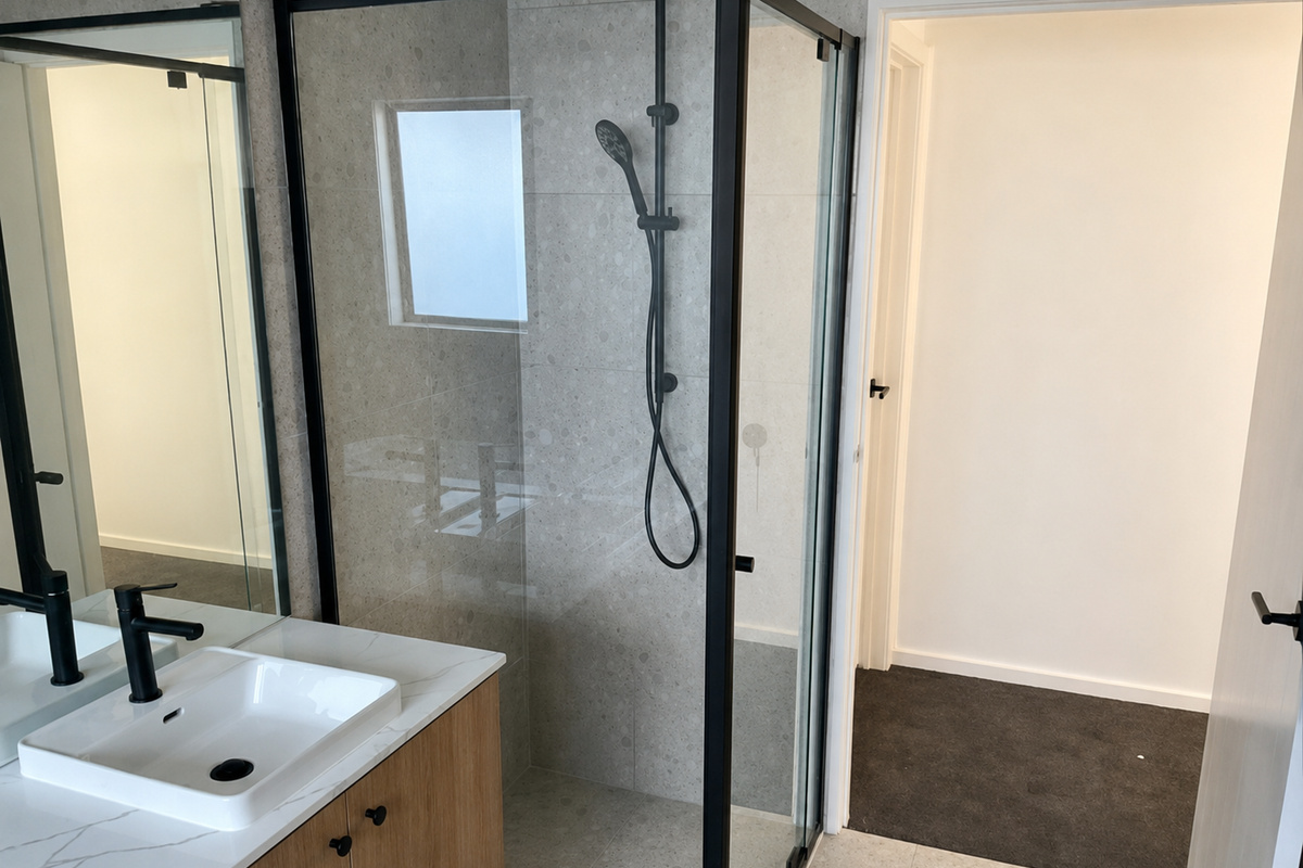 Ensuite with a glass-screened shower and black rail shower fittings, plus a timber vanity with basin and black tapware.