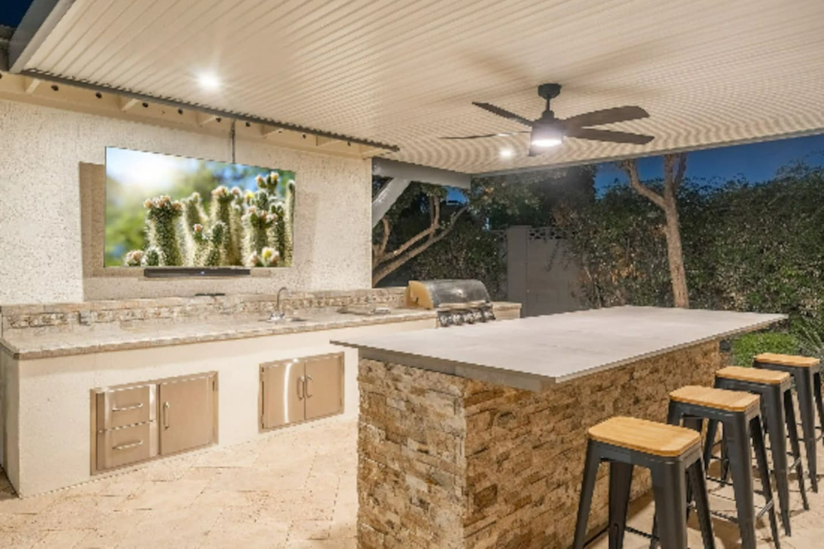 The outdoor bar seats the whole crew, with a built-in grill and big screen — this is where the party actually happens.