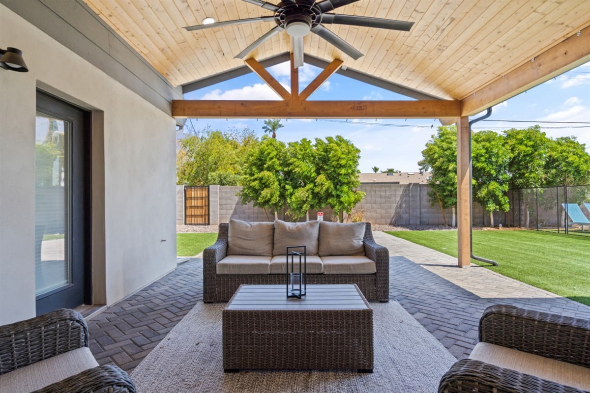 Shaded outdoor lounge with comfortable seating, ceiling fan, and easy access to the backyard.