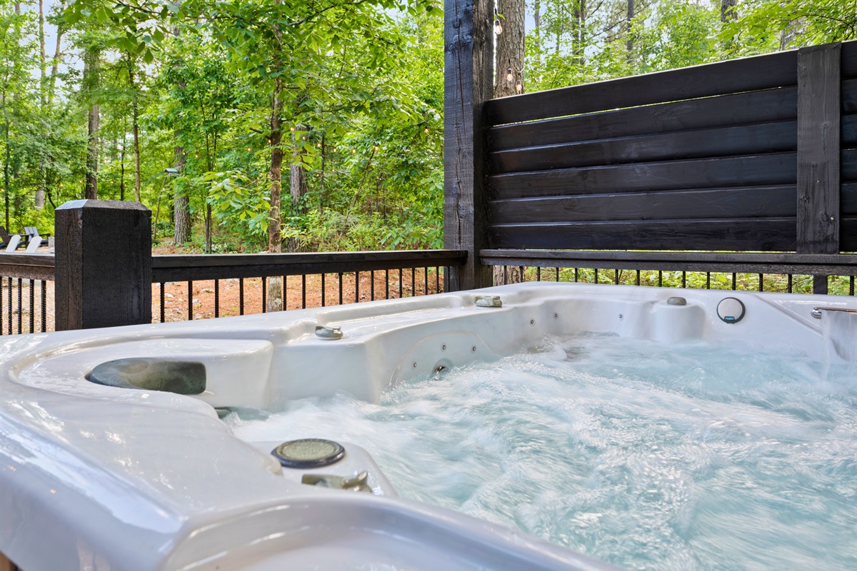 A hot tub with frothing water is nestled on a wooden deck surrounded by lush green trees