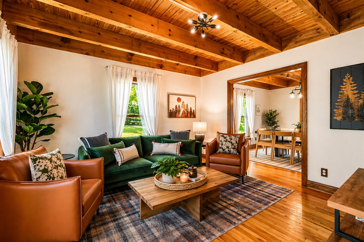 Exposed timber ceiling beams, green velvet sofa, leather armchairs, and a view straight through to the dining room — the living room is the center of the house and it earns it.