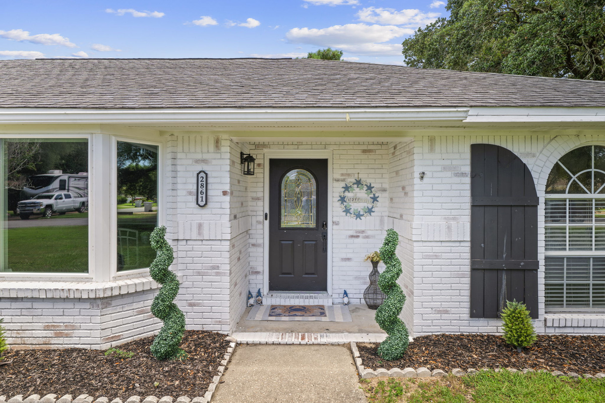 Step inside through this classic arched doorway, framed by manicured greenery and warm porch lighting.