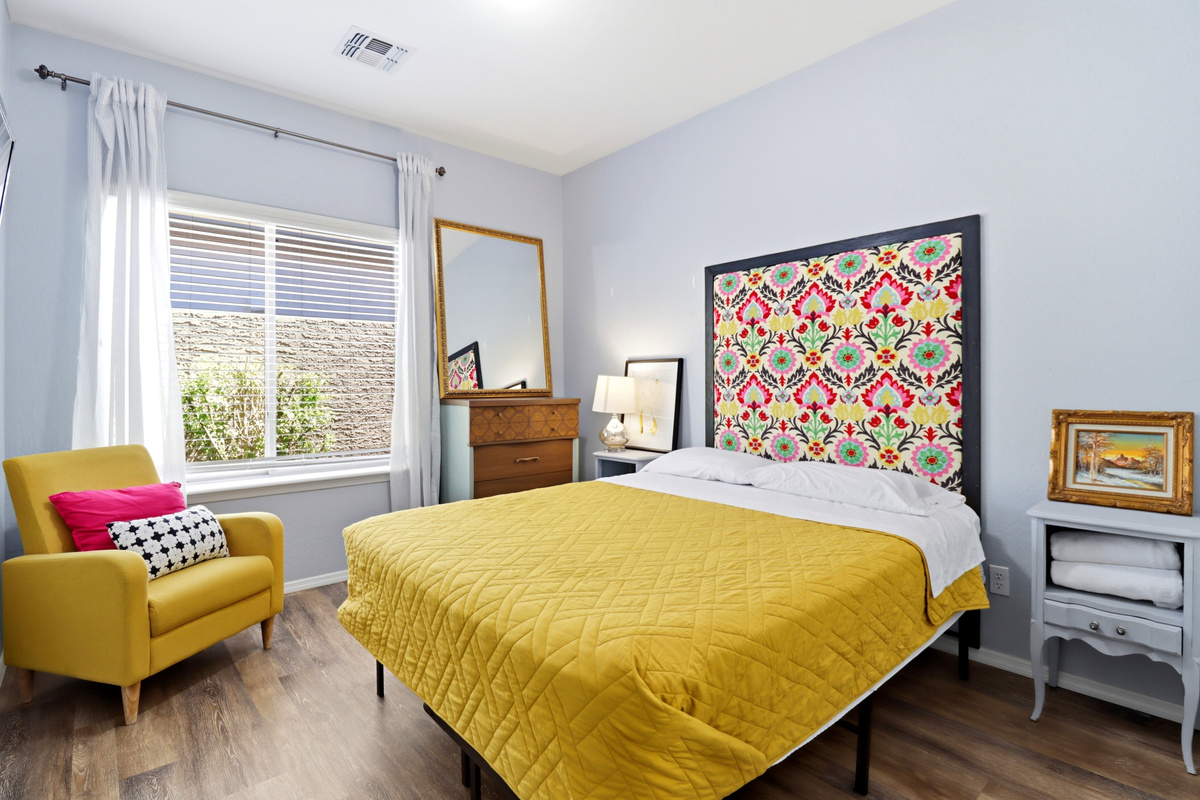 Queen bedroom with colorful bedding, a yellow accent chair, and a simple place to rest.
