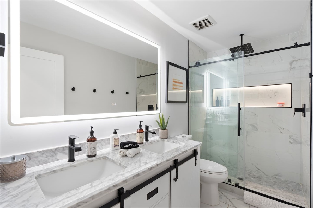 Sleek walk-in shower, dual-sink vanity, and glowing LED mirror for a luxe spa vibe.

