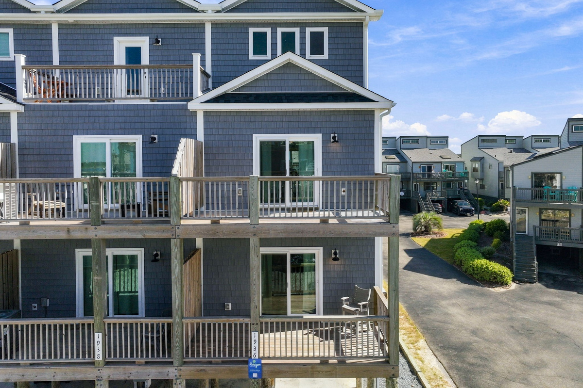 Close-up exterior perspective highlighting the multi-tiered wooden decks, sliding glass doors to individual rooms, blue-grey shaker siding, and neighborhood surroundings.