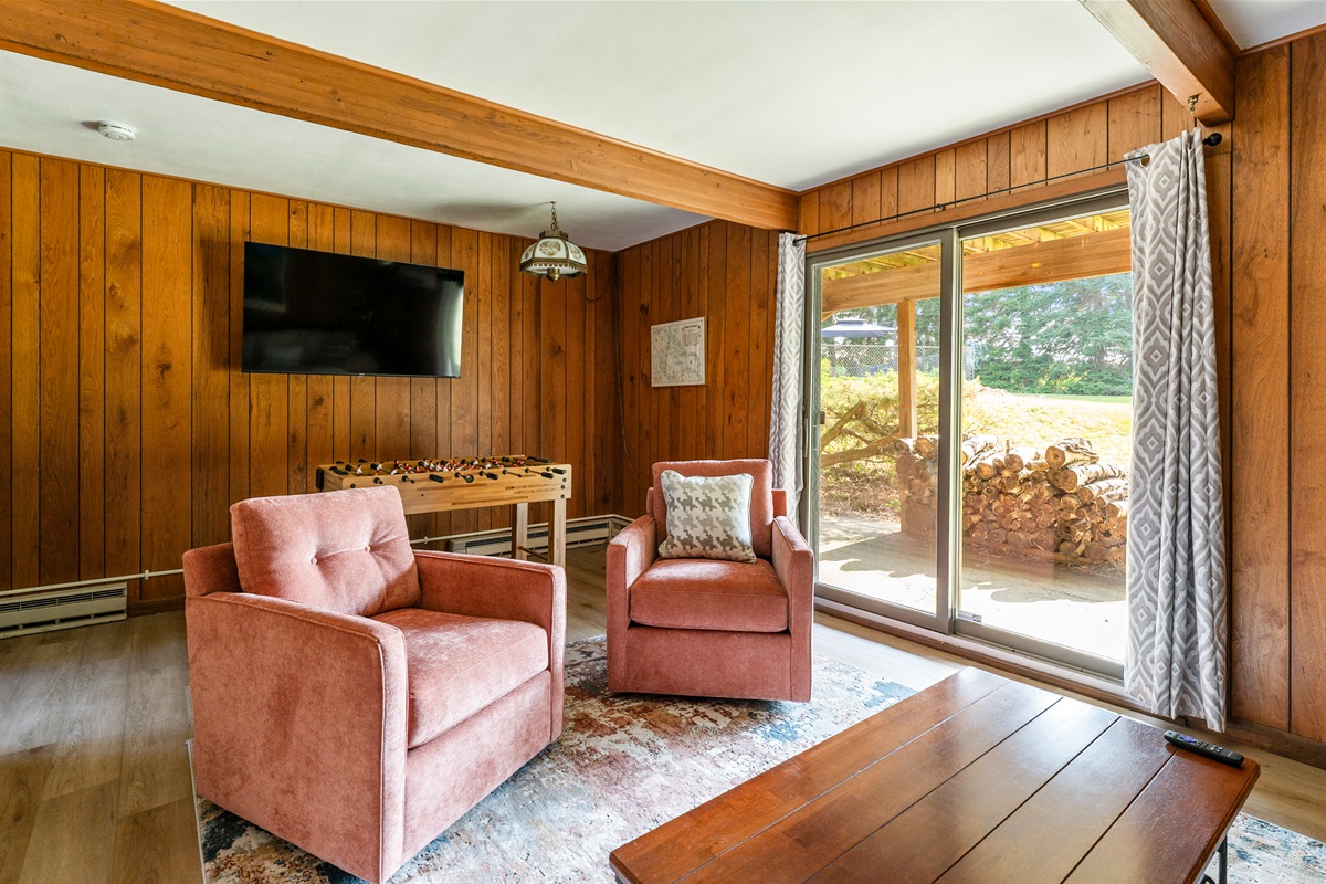 Bright and inviting lounge featuring comfy chairs, a large flat-screen TV, and sliding doors that open to the outdoors for a seamless indoor-outdoor retreat.