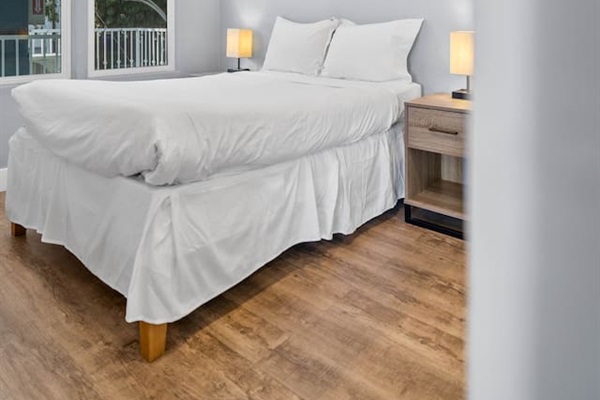Cozy bedroom featuring a thick, comfortable bed adorned with stylish lampshades on either side. Large windows offer a beautiful morning view, filling the room with natural light and creating a serene atmosphere for relaxation and rest.