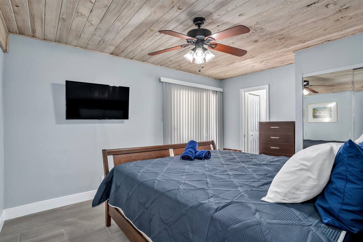 Master bedroom with King bed, private bathroom/shower. Smart TV, dresser, closet and ceiling fan as well as additional bathroom closet, and sliding glass door to patio area.