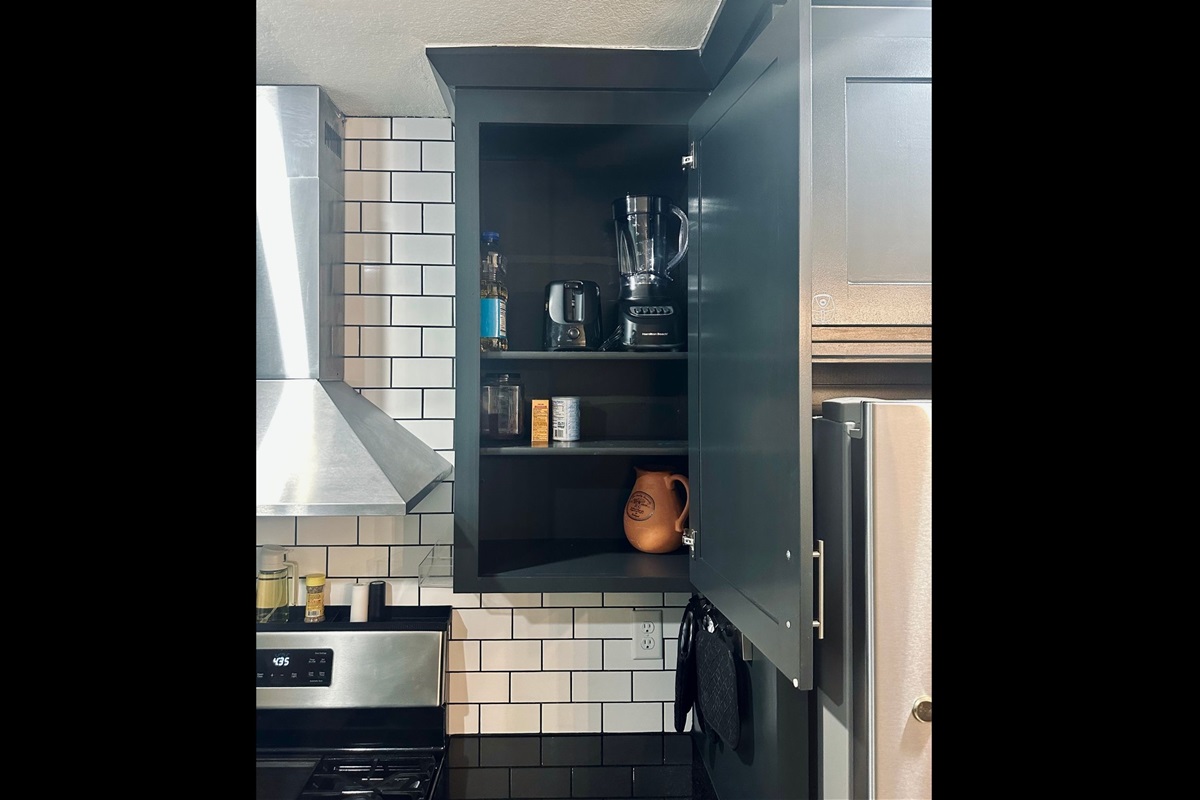 Kitchen cabinet featuring small appliances including a blender, toaster, and pitcher, along with essential cooking and baking staples.