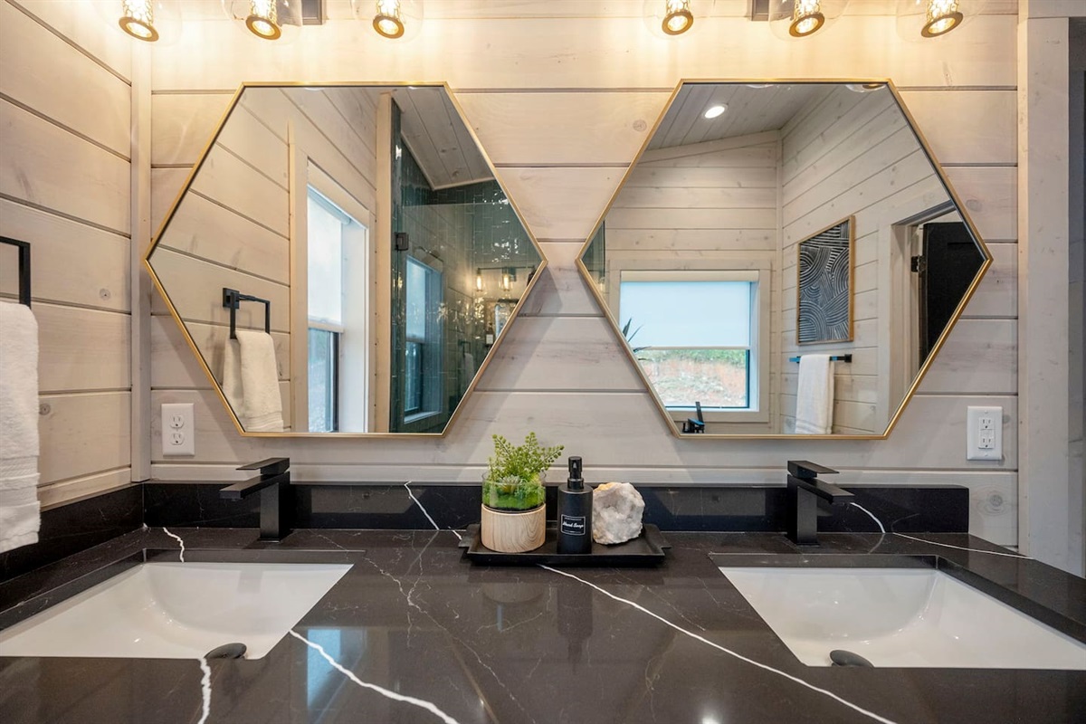 Primary bathroom vanity features double sinks, black quartz countertops and gold honeycomb mirrors.