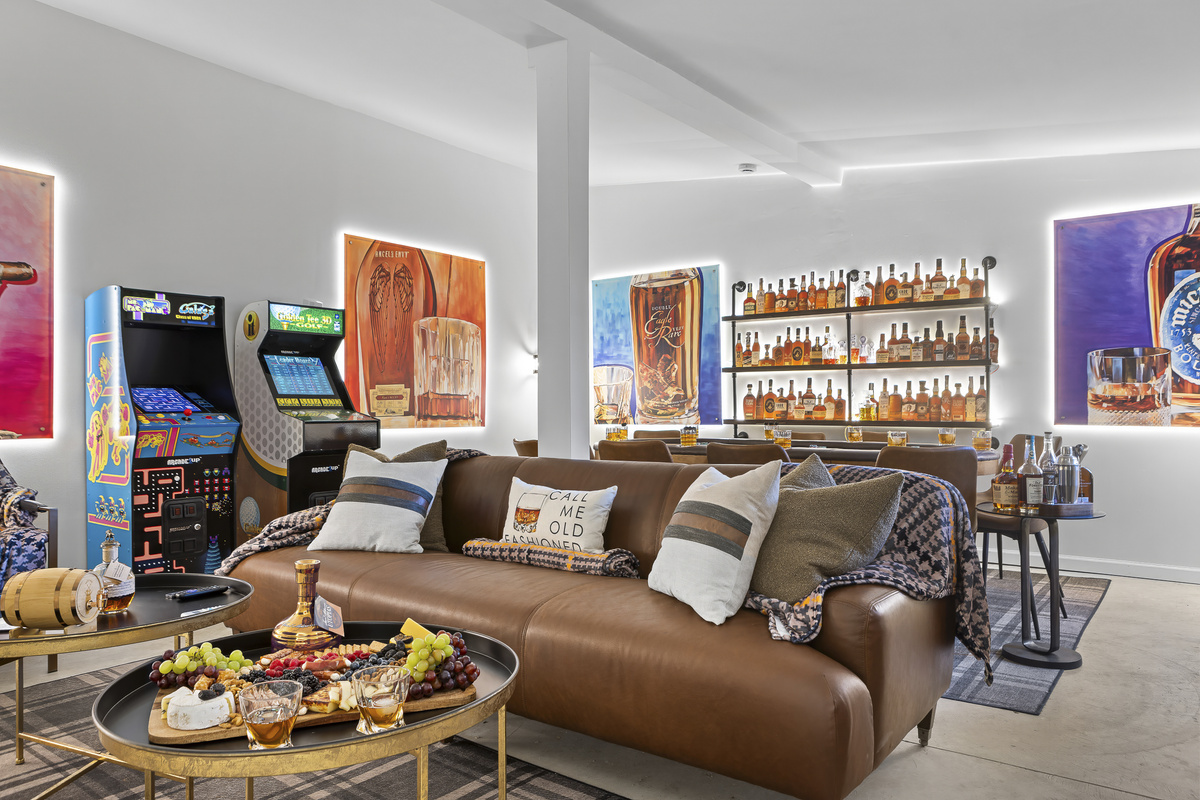 Your private game room awaits, featuring arcade machines, a full bourbon wall, shuffleboard, a poker table, and comfortable leather sofas for the whole crew.