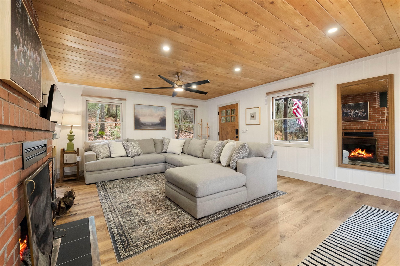 Spacious - yet cozy living room as you walk in. Showcasing a beautiful pine ceiling, lighting options, a large sofa, tv and wood burning fireplace.